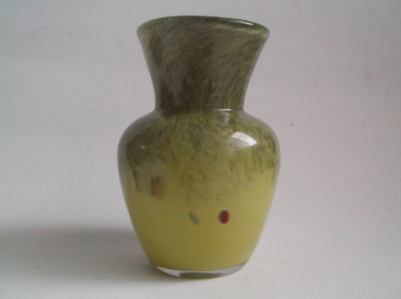 May include: A small, green and yellow glass vase with a mottled finish. The vase has a round body and a narrow neck.