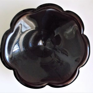 May include: A black glass bowl with a scalloped edge. The bowl is shiny and reflects light.