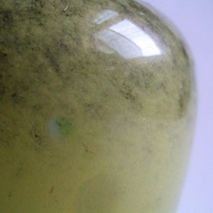 May include: A close-up of a green glass bottle with a textured surface. The bottle is slightly cloudy and has a few small imperfections.