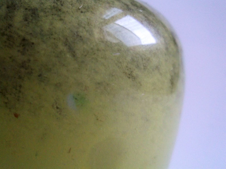 May include: A close-up of a green glass bottle with a textured surface. The bottle is slightly cloudy and has a few small imperfections.