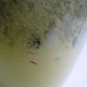 May include: A close-up of a light green glass vase with a textured surface. The vase has a white, gray, and blue design with a red accent.