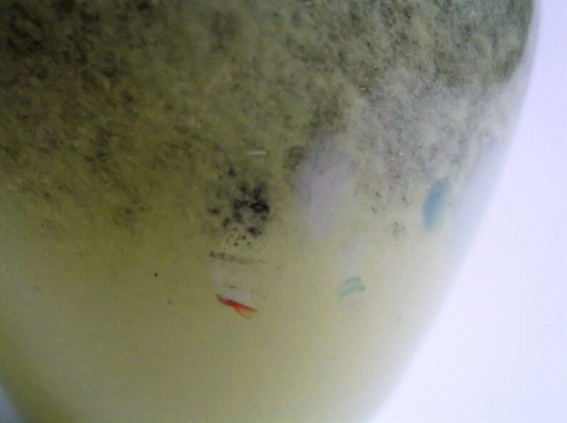 May include: A close-up of a light green glass vase with a textured surface. The vase has a white, gray, and blue design with a red accent.