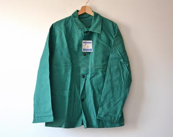 May include: A solid green long-sleeve jacket featuring a pointed collar, a front button closure with dark buttons, and a chest pocket. A small white rectangular tag with blue text is attached to the front of the jacket near the chest area.
