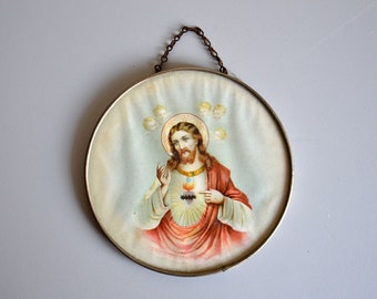 May include: A round, framed picture of Jesus Christ with a golden halo and a red robe. The picture is surrounded by a silver frame and has a chain for hanging.