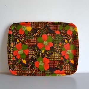 Peut inclure: Un plateau de service rectangulaire présentant un fond brun foncé avec un motif répétitif de fleurs orange vif et vertes. Le design comprend de petits accents géométriques jaunes et orange dispersés à travers le motif floral.