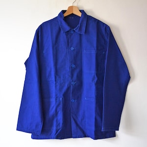 Peut inclure: Une veste de travail bleu vif avec une fermeture boutonnée, deux poches de poitrine et deux poches inférieures. La veste est suspendue à un cintre en bois sur un fond blanc. La veste à manches longues est en tissu résistant.