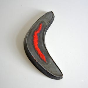 May include: A gray ceramic boomerang with a red stripe down the center.