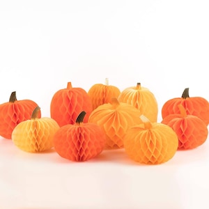 May include: A collection of ten decorative honeycomb paper pumpkins in various shades of orange and yellow. Each pumpkin features a textured, expandable paper structure and a small, dark-coloured stem at the top, arranged in a cluster.