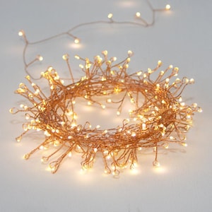Op de afbeelding: Koperen draad lichtsnoer met warm witte LED-lampjes. De lampjes zijn in een verwarde, ronde vorm aan elkaar geregen.