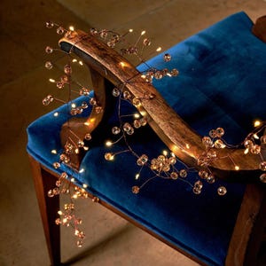Op de afbeelding: Een decoratieve lichtsnoer met een dunne, koperkleurige draad versierd met kleine, doorzichtige, bolvormige kralen. De flexibele draad is verlicht door kleine, warmgekleurde LED-lampjes die tussen de kralen zijn geplaatst voor een gloeiend effect.