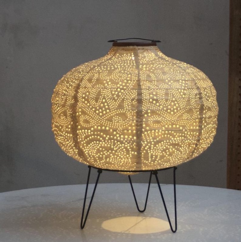 Op de afbeelding: Een witte keramische lamp met een delicaat patroon en een zwarte metalen standaard. De lamp is verlicht en geeft een warm licht.