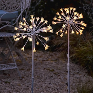 以下が含まれることがあります： 星型の屋外用装飾ライト2つ。各ライトは、小さな温白色のライトが付いた放射状の茎を持つ中央の球体を持っています。茎は灰色のポールで支えられており、ぼやけた屋外の背景に設置されています。