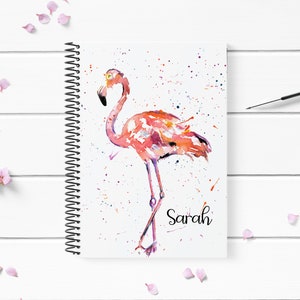 May include: A watercolour painting of a pink flamingo on a white background with colourful paint splatters. The name "Sarah" is written in black cursive at the bottom of the image.