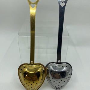 May include: Two heart-shaped tea infusers with long handles. One infuser is gold and the other is silver.