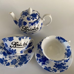 May include: A blue and white floral tea set with a teapot and two teacups and saucers. The teapot and cups are decorated with the word "Bristol" in black lettering.