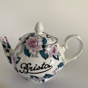 Pu&ograve; includere: Teiera bianca con un motivo floreale di rose rosa e foglie verdi. La teiera ha un'iscrizione nera che recita "Bristol".