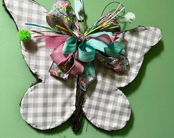 May include: A gray and white gingham butterfly wreath with a floral ribbon and a green bow. The wreath is decorated with a variety of colorful ribbons and flowers.