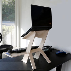 May include: A light wood laptop stand with a black laptop on top. The stand has a shelf for a keyboard and mouse. The stand is on a black desk.