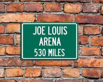 Puede incluir: Un letrero verde con texto blanco que dice "Joe Louis Arena 530 Miles" montado en una pared de ladrillo.