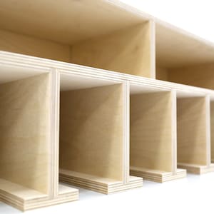 May include: A close-up of a wooden shelf unit with multiple compartments. The shelf is made of light-colored wood and has a simple, modern design.