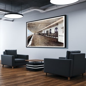 Op de afbeelding: Een zwart-witfoto van een scheepsdek, ingelijst en hangend aan een muur in een moderne kantooromgeving. Twee zwarte fauteuils en een salontafel staan voor het beeld.