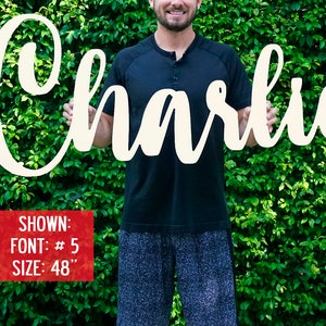 May include: A white wooden sign with the name "Charlie" written in a cursive font. The sign is 48 inches tall and is being held by a person. The sign is shown in font #5.