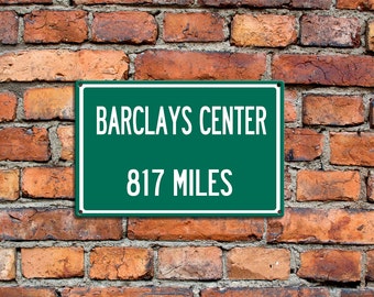 Puede incluir: Un letrero verde con texto blanco en una pared de ladrillo. El letrero dice "Barclays Center 817 Miles".