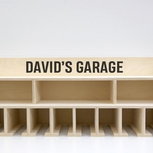 May include: A wooden wall-mounted storage shelf with the text "DAVID'S GARAGE" on the top shelf. The shelf has 12 compartments and is made of light wood.