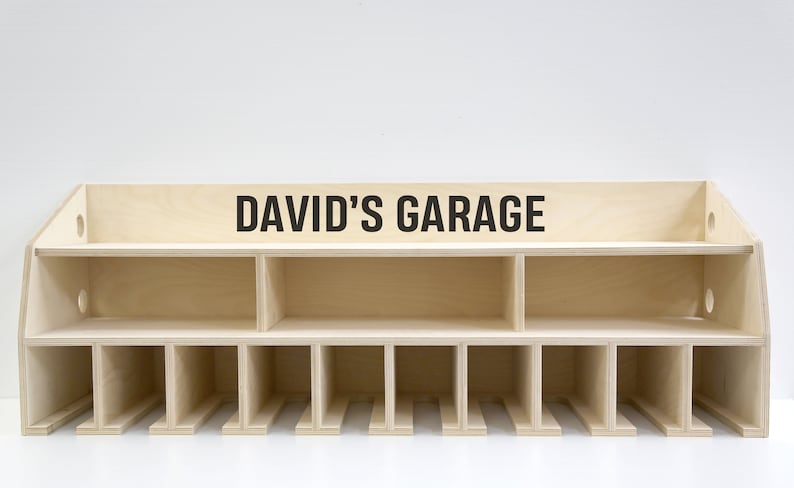 May include: A wooden wall-mounted storage shelf with the text "DAVID'S GARAGE" on the top shelf. The shelf has 12 compartments and is made of light wood.