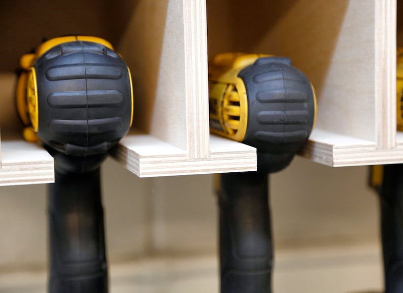May include: Close-up of three yellow and black cordless drills stored in a wooden rack. The drills are held in place by the rack's design, which allows for easy access and organization.