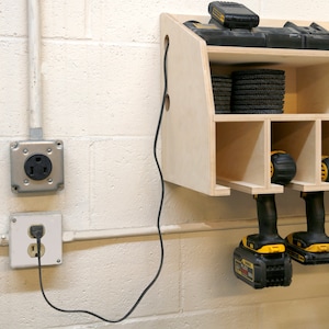 May include: A wall-mounted wooden storage unit with shelves for tools and accessories. The unit has a power outlet and a cord running to it. There are two cordless drills hanging from the bottom of the unit.