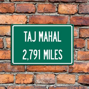 May include: A green sign with white text that reads "TAJ MAHAL 2,791 MILES" mounted on a brick wall.