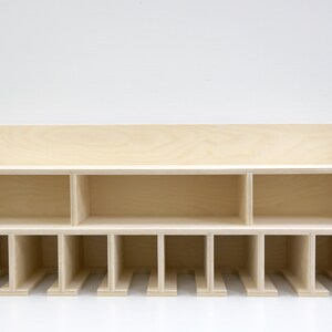 May include: A wooden wall-mounted shelf with multiple compartments. The shelf has a light wood finish and is divided into 12 sections, with a larger shelf on top.