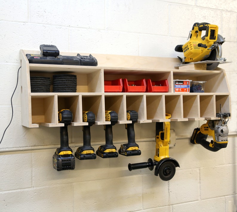 May include: A wooden wall-mounted storage unit with multiple compartments for organizing tools. It features a variety of power tools, including drills, a saw, and a sander, all in yellow and black. The unit also includes red plastic storage bins and a variety of sanding discs.