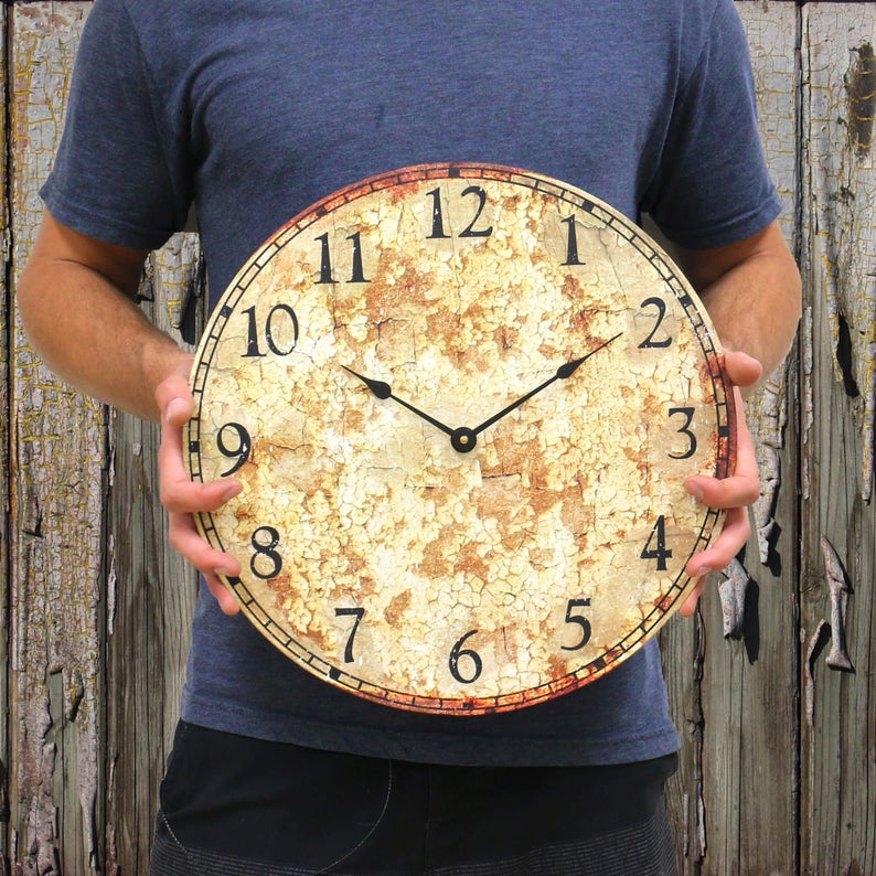 Puede incluir: Una esfera de reloj blanca y marr&oacute;n desgastada con n&uacute;meros romanos negros y agujas negras. La esfera del reloj tiene un aspecto agrietado y envejecido.