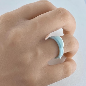 May include: A light blue ring with a unique design. The ring is made of a smooth, glossy material and has a slightly curved shape.