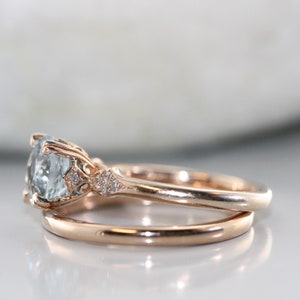 May include: A rose gold engagement ring with a large, light blue gemstone surrounded by smaller diamonds. The ring is paired with a matching rose gold wedding band.