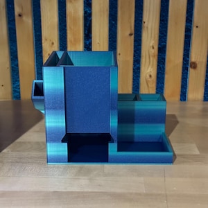 May include: A multi-compartment desk organizer in shades of blue and teal. The organizer has several sections, including a pen holder, a small tray, and a larger compartment. The item is made of a solid material and sits on a wooden surface.
