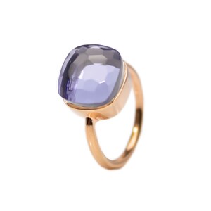 Puede incluir: Un anillo de oro rosa con una gran gema de color lavanda, de corte cuadrado. La gema está engastada en un bisel, y la banda tiene un diseño simple y pulido.