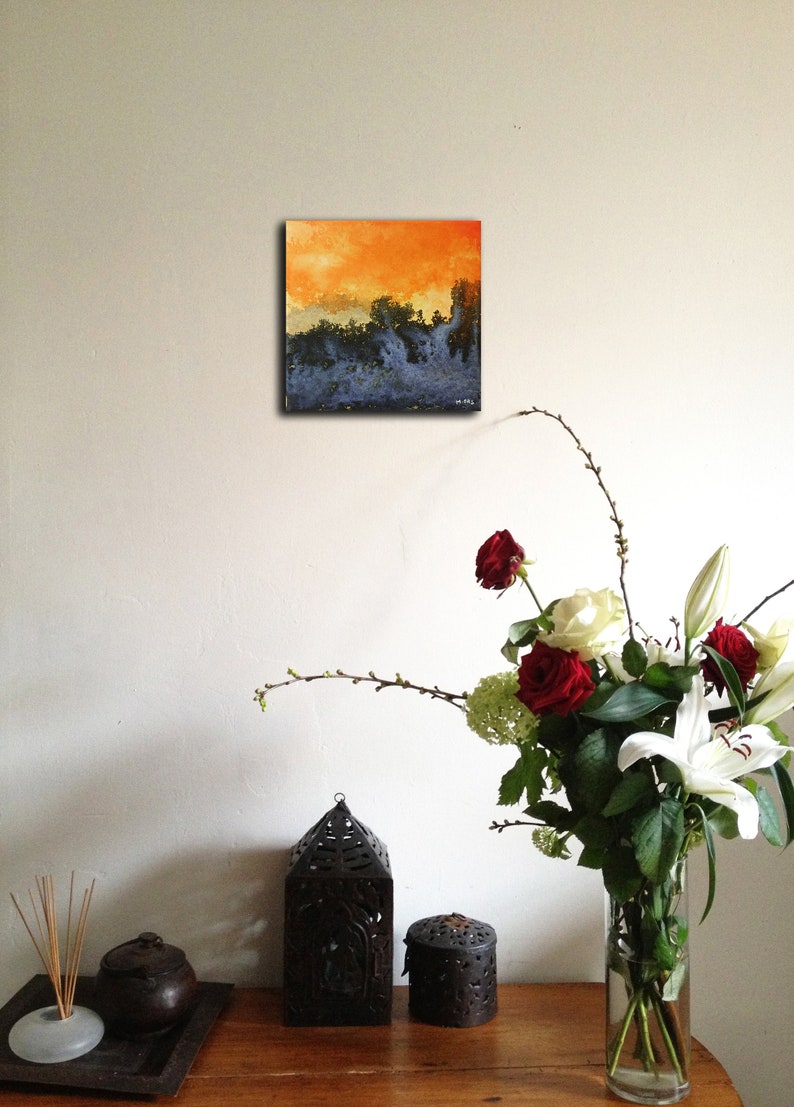 May include: A small abstract painting with a blue and orange color scheme. The painting is hanging on a white wall above a table with a vase of flowers and decorative objects.