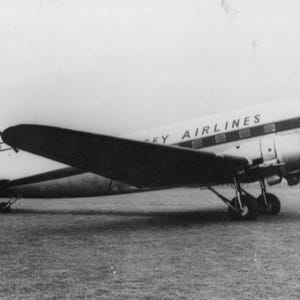 May include: Black and white image of a vintage airplane on a grassy field. The plane has the words "Jersey Airlines" printed on the side. The plane has two propellers and is in good condition.