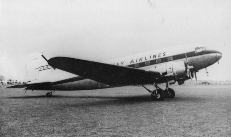 May include: Black and white image of a vintage airplane on a grassy field. The plane has the words "Jersey Airlines" printed on the side. The plane has two propellers and is in good condition.