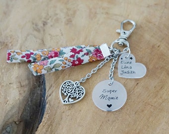 May include: A keyring featuring a silver lobster clasp, two floral fabric strips, a heart-shaped tree charm, and two silver-toned discs. One disc is engraved with Super Mamie and a heart, the other with the names Eline, Léna, and Judith.