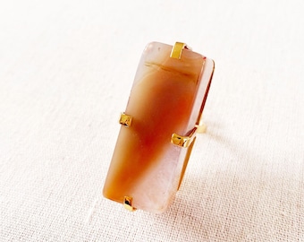 Può includere: Un anello d'oro con una pietra di agata rettangolare. La pietra è una miscela di bianco e marrone.