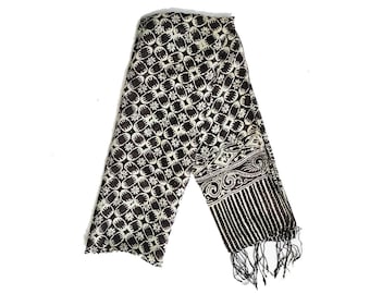 May include: A brown and white patterned scarf with a fringe. The scarf has a geometric design with a floral motif.