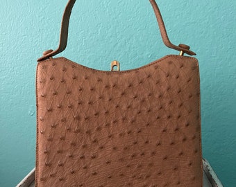 May include: A brown ostrich leather handbag with a gold clasp and top handle.