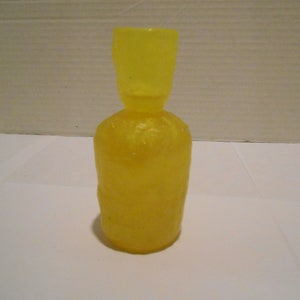 May include: A yellow glass bottle with a textured surface. The bottle has a narrow neck and a wide base.