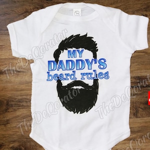 May include: White baby onesie with blue text that reads "My Daddy's beard rules" and a black silhouette of a man's face with a beard.