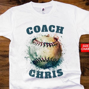 Könnte beinhalten: Weißes T-Shirt mit einem Aquarell-Baseball-Design und dem Text "COACH CHRIS" in dunkelblau.