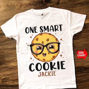 May include: White t-shirt with a cartoon cookie wearing glasses and the text "One Smart Cookie Jackie".